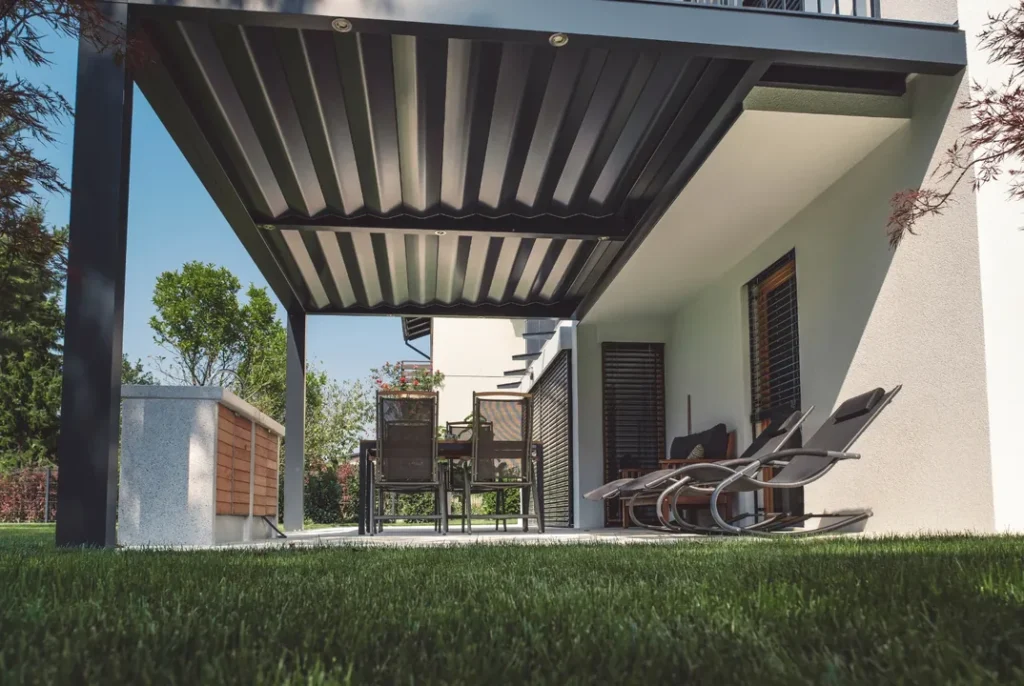 Pérgola bioclimática de lamas orientables vista desde un jardín con zona de descanso