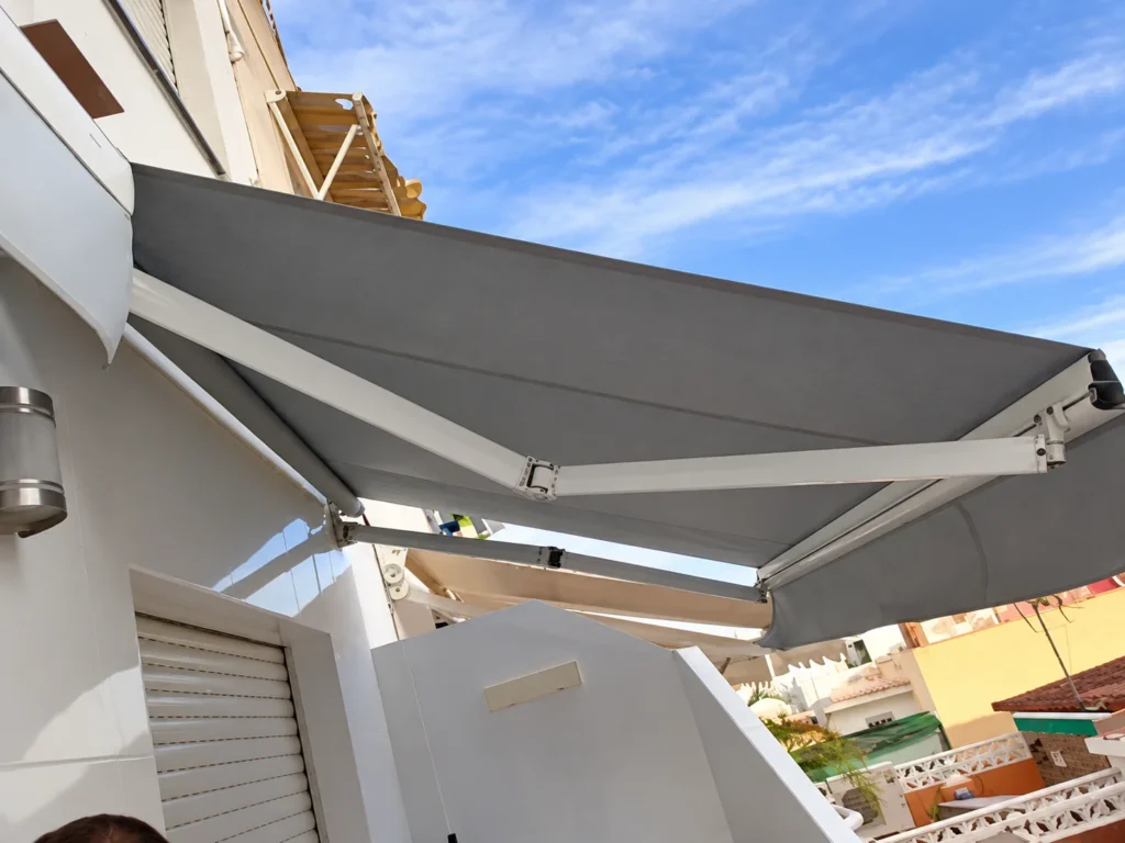 Toldos para balcones en Madrid: toldo extensible de lona gris con brazos instalado en una vivienda