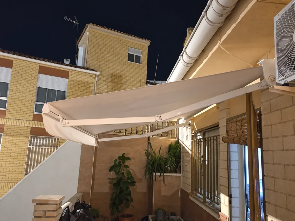 Toldo extensible de lona beige sobre un patio con fachada de ladrillo en Madrid