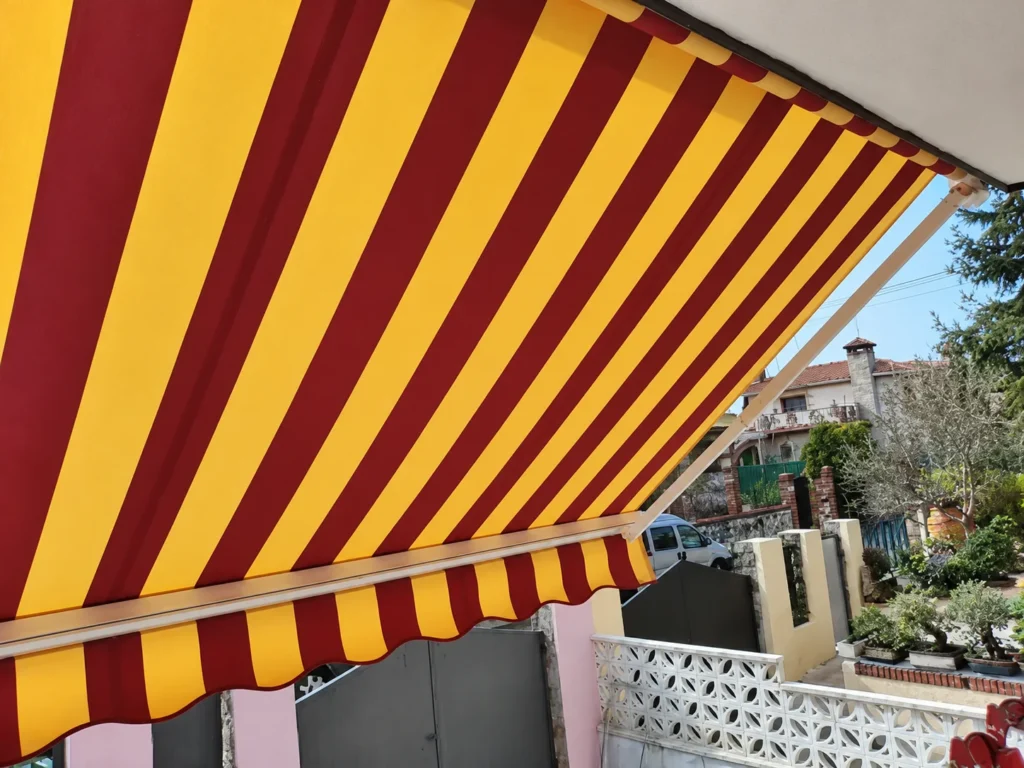 Toldos para balcones en Madrid: toldo de rayas rojas y amarillas con volante en una fachada