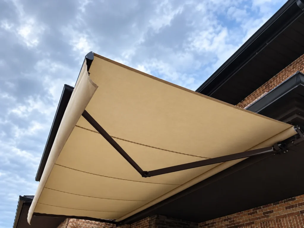 Toldos para balcones en Madrid: toldo extensible beige con brazos oscuros en una fachada de ladrillo