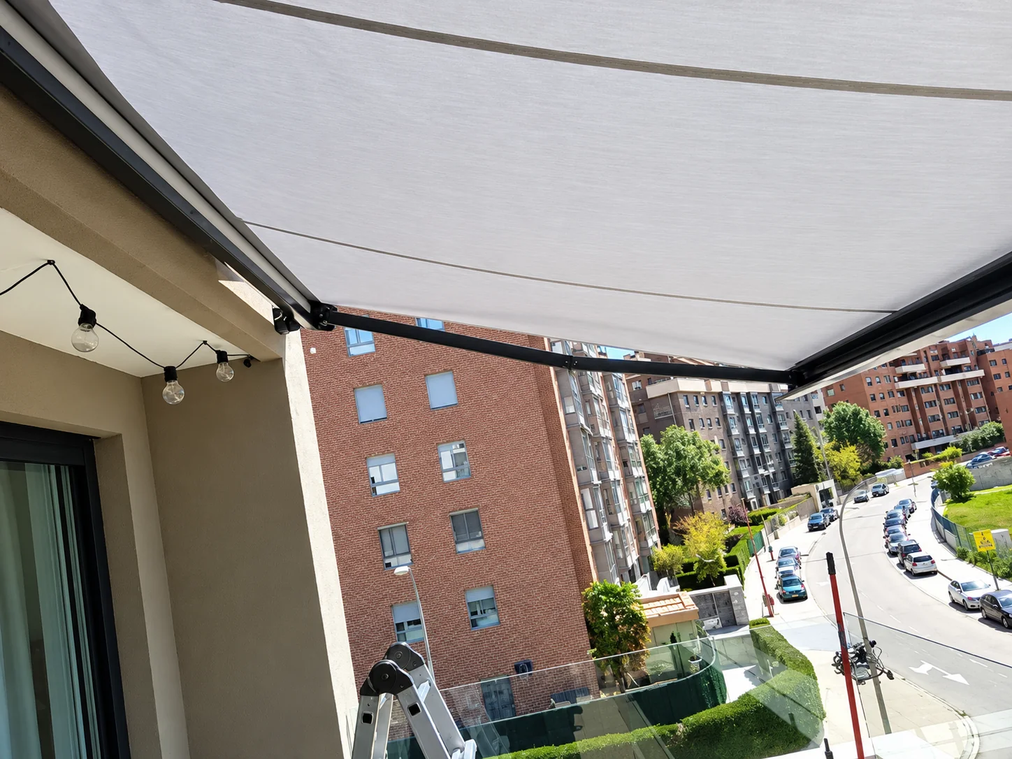 Toldos para balcones en Madrid: toldo extensible de lona clara con vistas a la calle desde un balcón