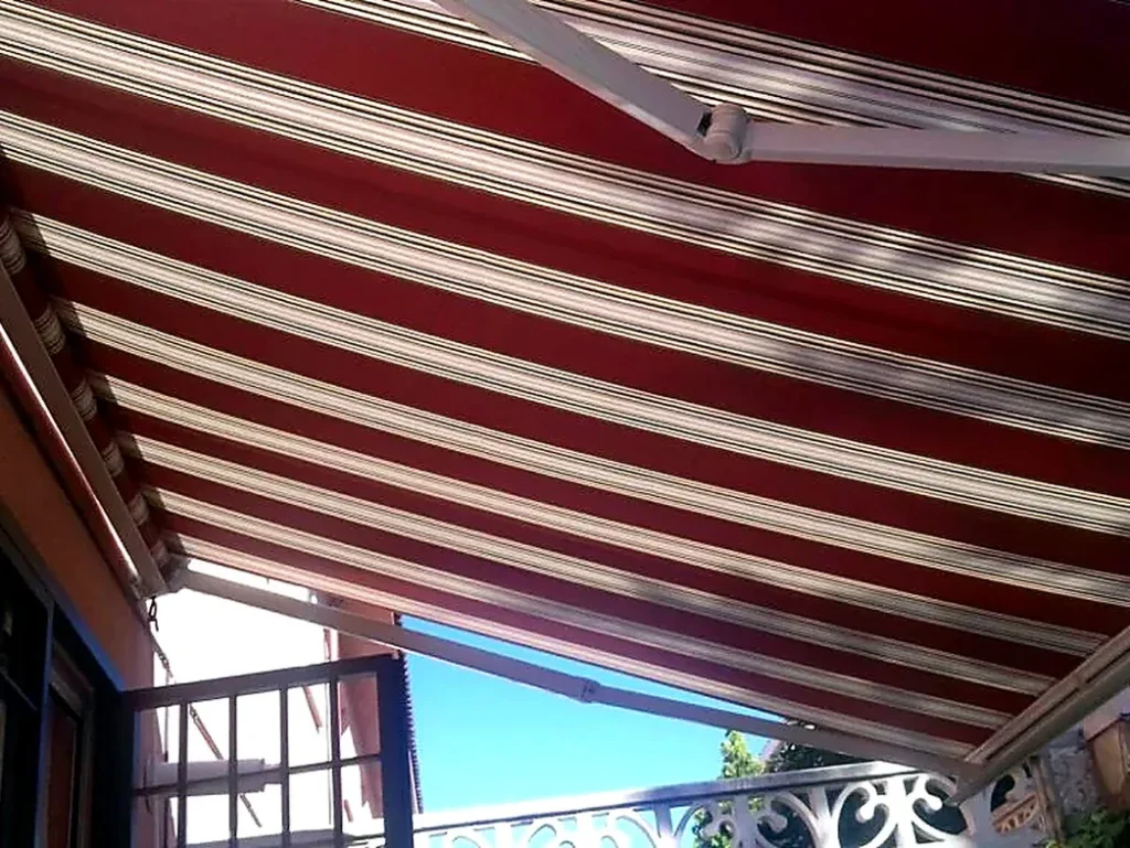 Toldos para terrazas en Madrid: toldo de rayas granate sobre terraza con barandilla