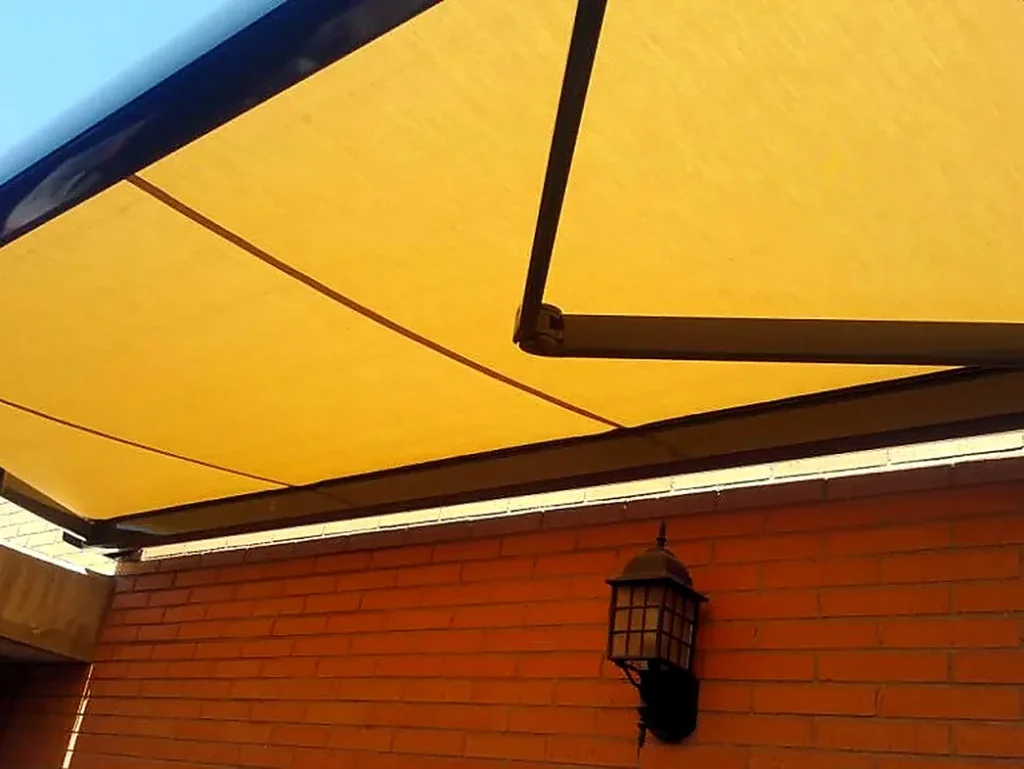 Toldos para terrazas en Madrid: toldo amarillo con brazo articulado junto a fachada