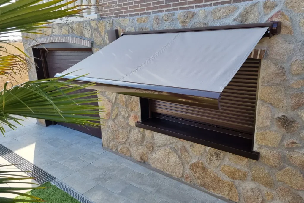 Toldo para ventana de color gris sobre persiana en una fachada de piedra