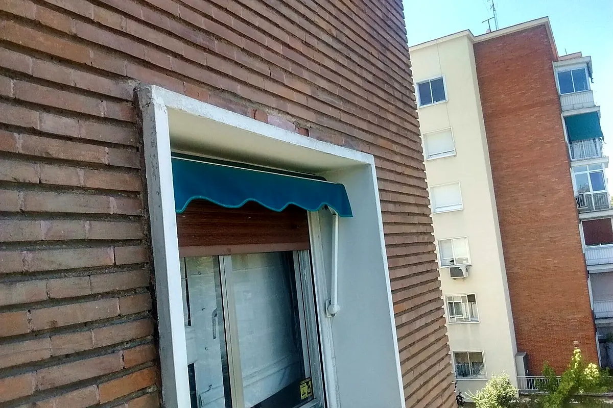 Toldo para ventana con volante azul en una fachada de ladrillo