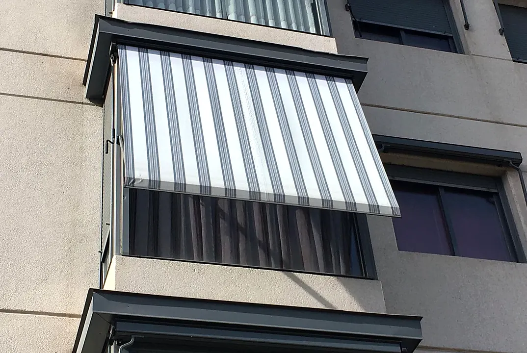Toldo de rayas grises y blancas en la ventana de un balcón