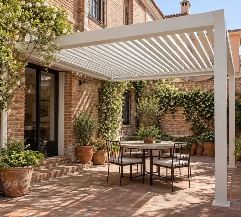 Pérgola bioclimática blanca con lamas orientables sobre un patio de ladrillo y terracota