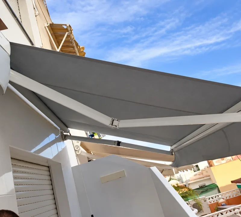 Toldos para balcones en Madrid: toldo extensible de lona gris con brazos instalado en una vivienda