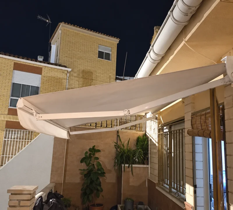 Toldo extensible de lona beige sobre un patio con fachada de ladrillo en Madrid