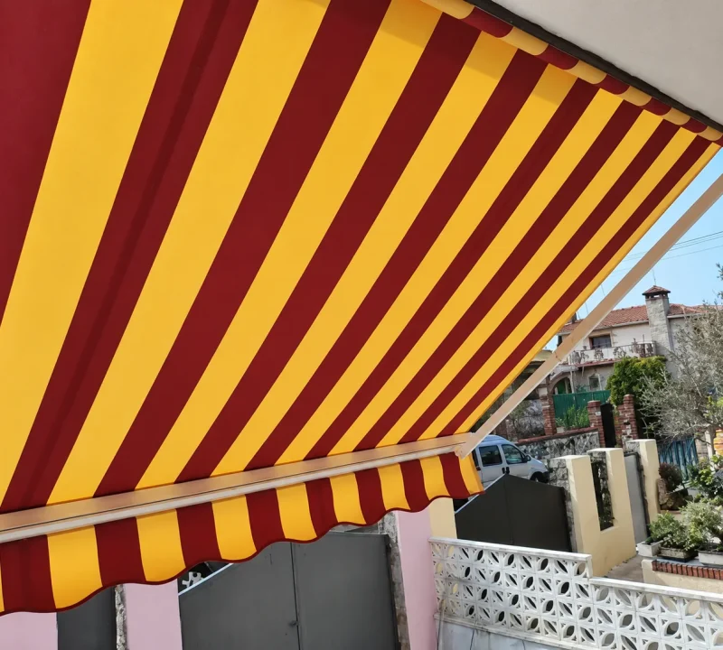 Toldos para balcones en Madrid: toldo de rayas rojas y amarillas con volante en una fachada