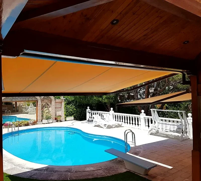 Toldos para terrazas en Madrid: toldo naranja bajo estructura de madera junto a la piscina