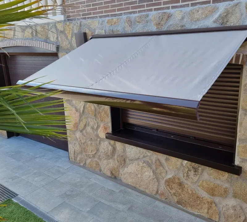 Toldo para ventana de color gris sobre persiana en una fachada de piedra